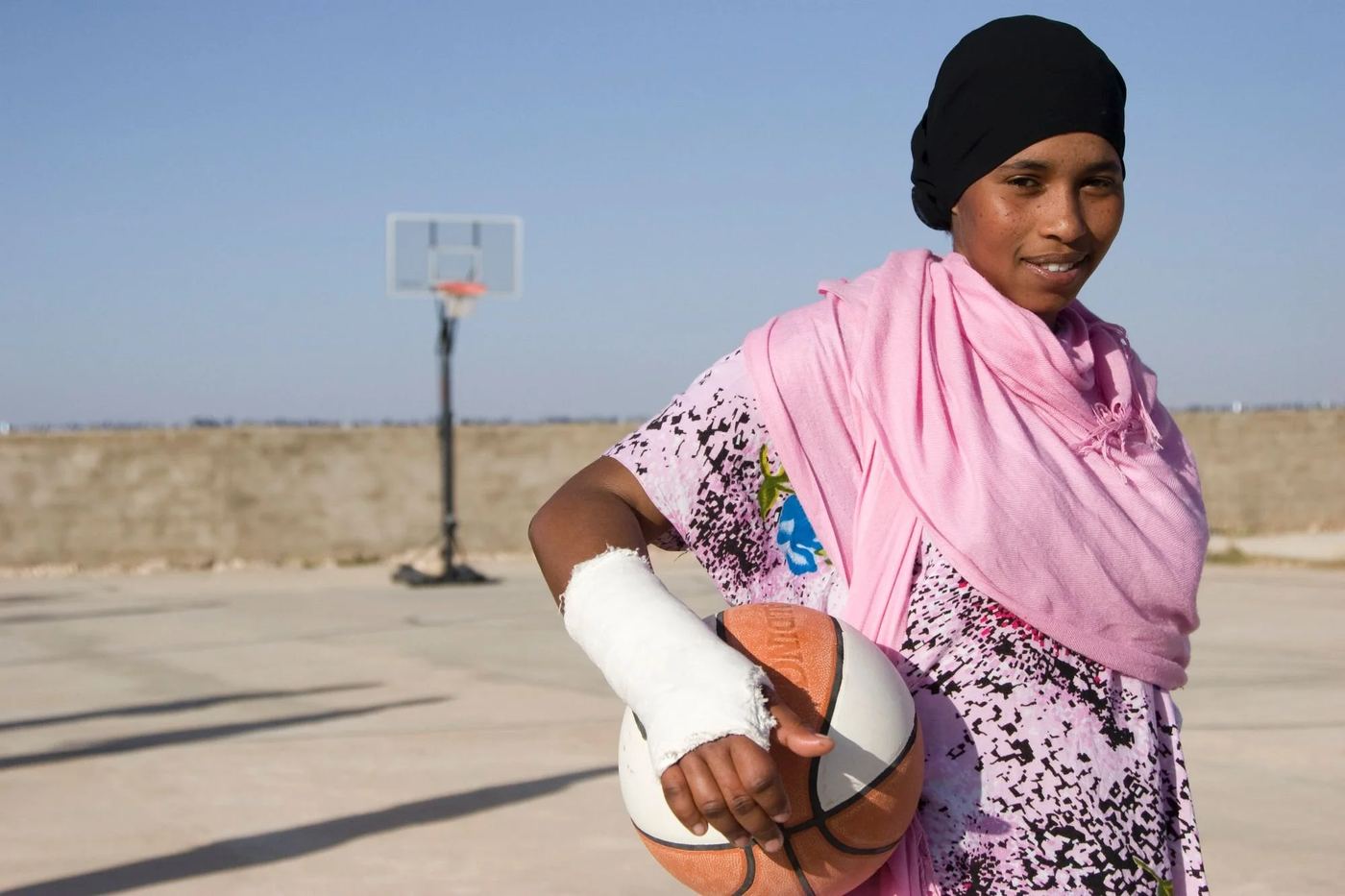 An Abaarso student holding a basketball on an outdoor court, smiling at the camera.